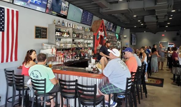 Bar with patrons seated on stools, American flag on the wall, and bottles displayed behind the counter.