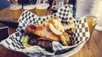 Basket of wings and potato wedges on a wooden table with drinks in the background