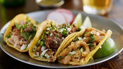 Plate of three beef tacos with lime wedges and radish slices on a dark table