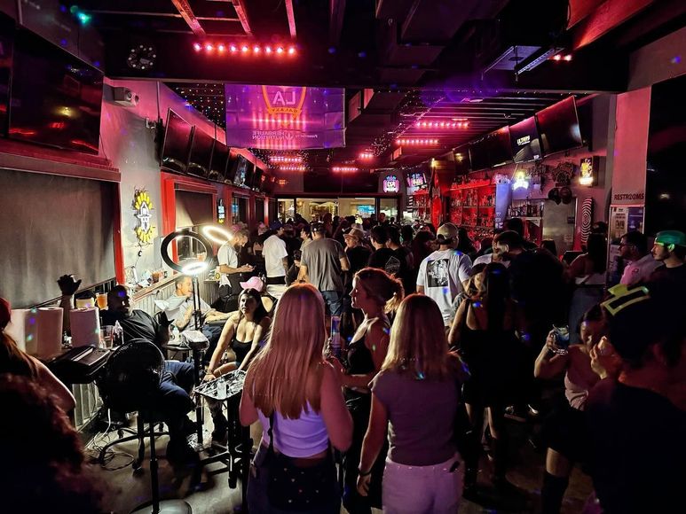 Crowded nightclub with colorful pink and purple lights, people dancing and socializing near a stage