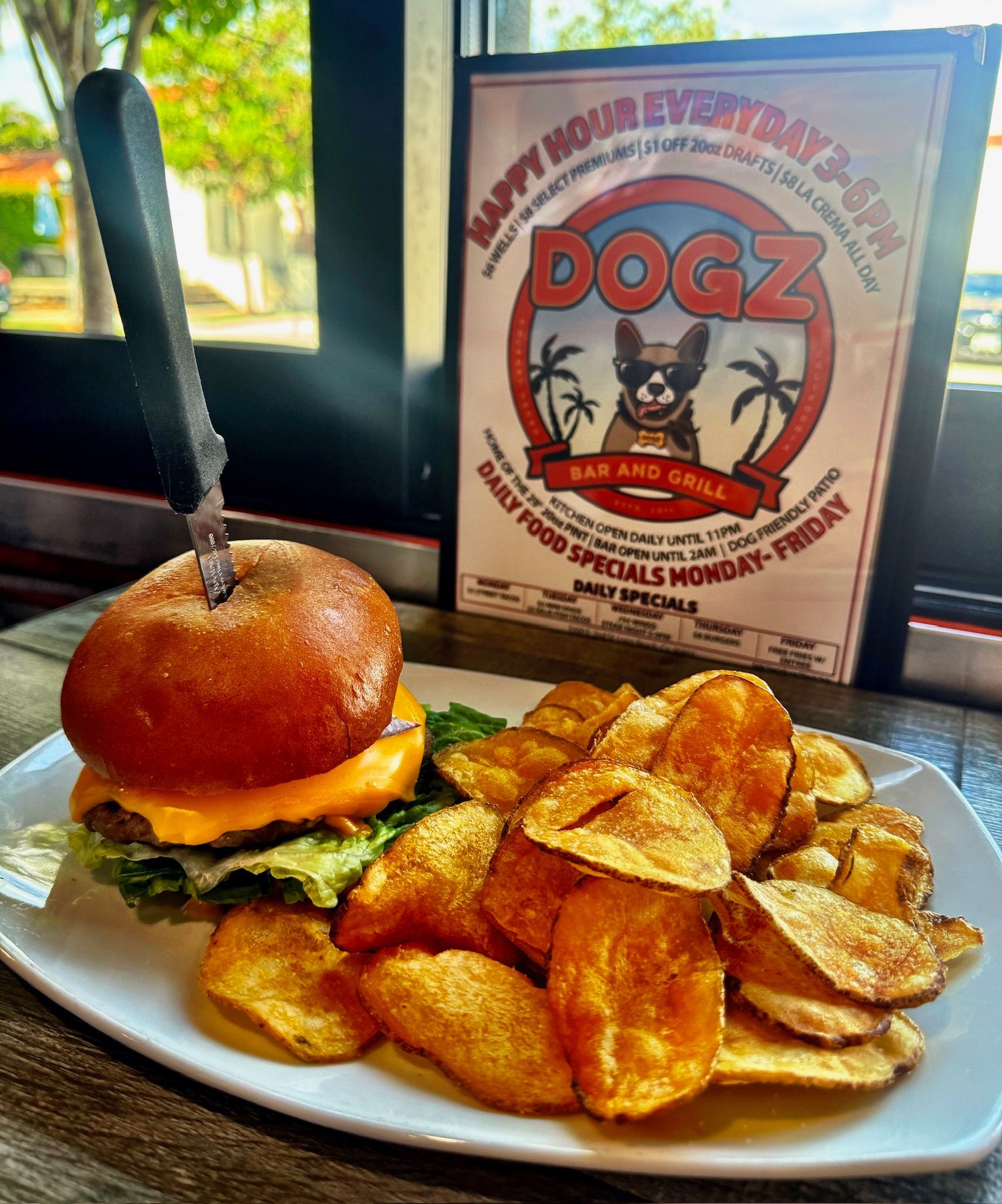Burger and chips on a white plate beside a DOGZ menu sign in a restaurant booth