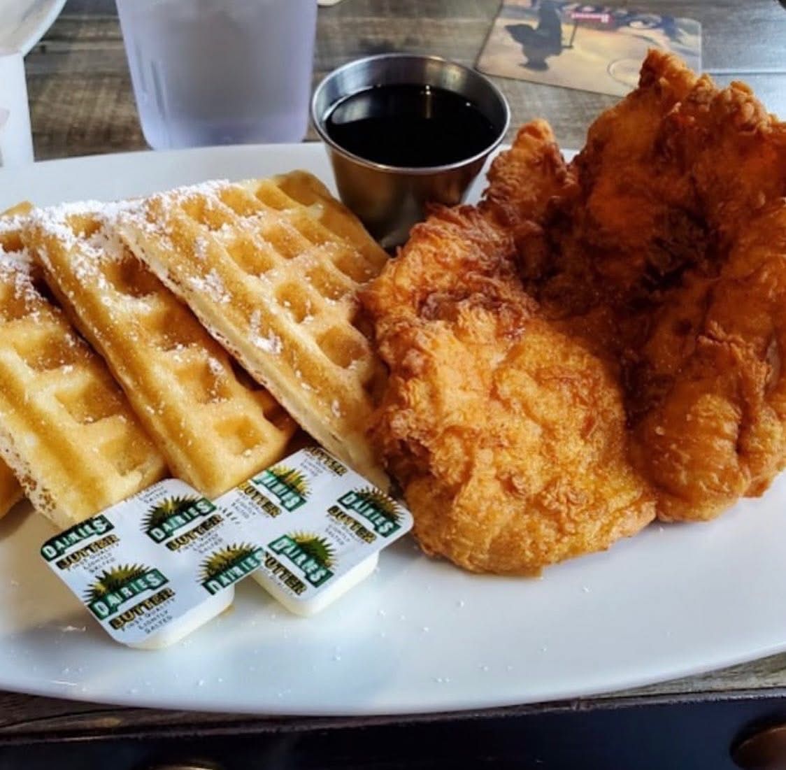 Waffles with syrup packets and fried chicken on a white plate