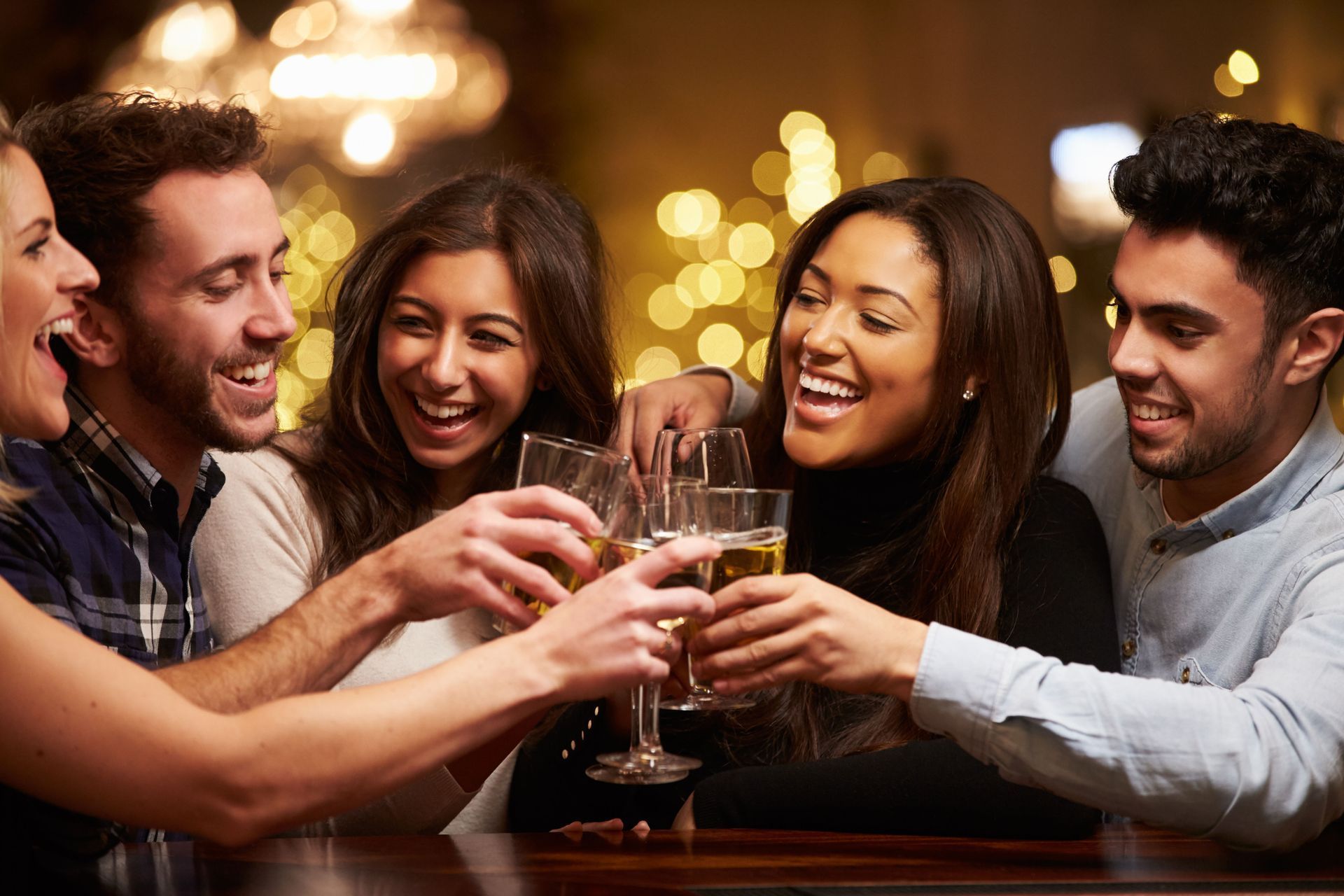Friends smiling and clinking drinks at a warmly lit bar or restaurant