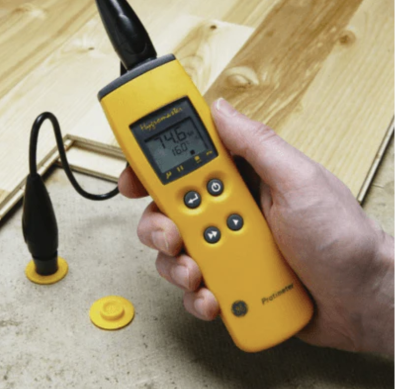 Hand holding a yellow digital meter beside probes on a wooden table.
