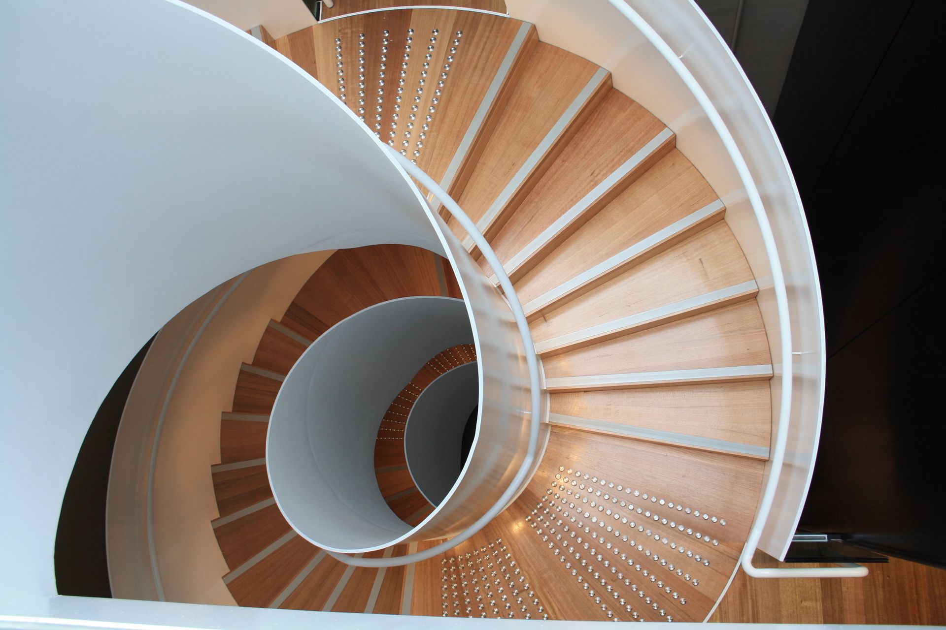 Spiral wooden staircase with white curved walls and a central circular opening — Unique Floors In New Town, TAS