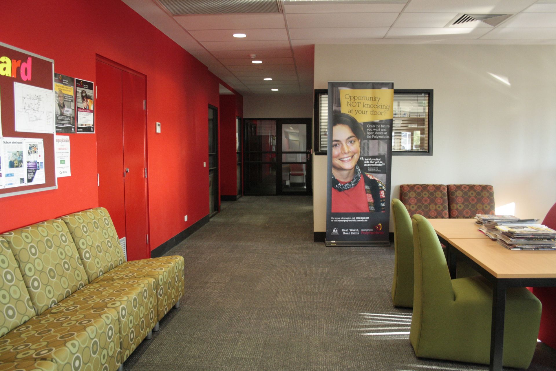 Waiting area with green chairs, red walls, a table, and a poster stand in a hallway — Unique Floors In New Town, TAS