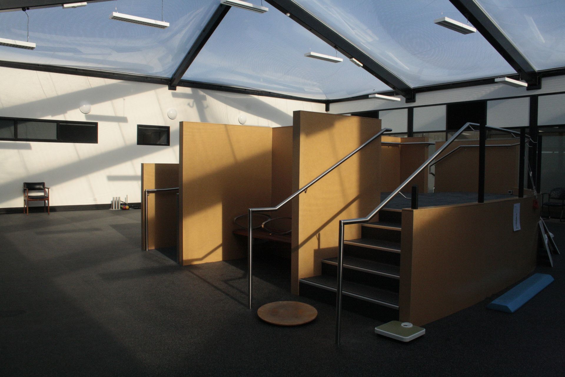 Empty indoor mini-golf area with black flooring, brown partition walls, and a staircase