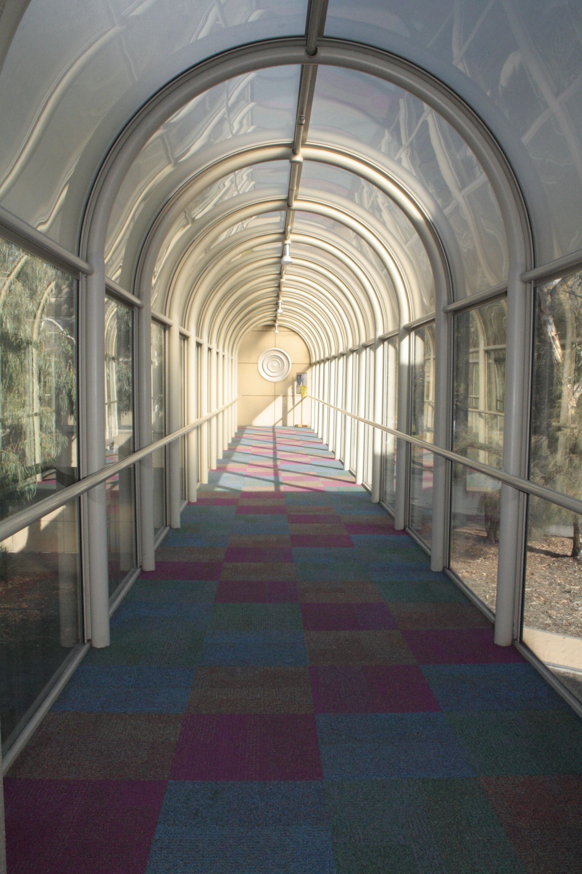 Covered walkway with arched glass tunnel, colorful carpet, and sunlight at the far end — Unique Floors In New Town, TAS