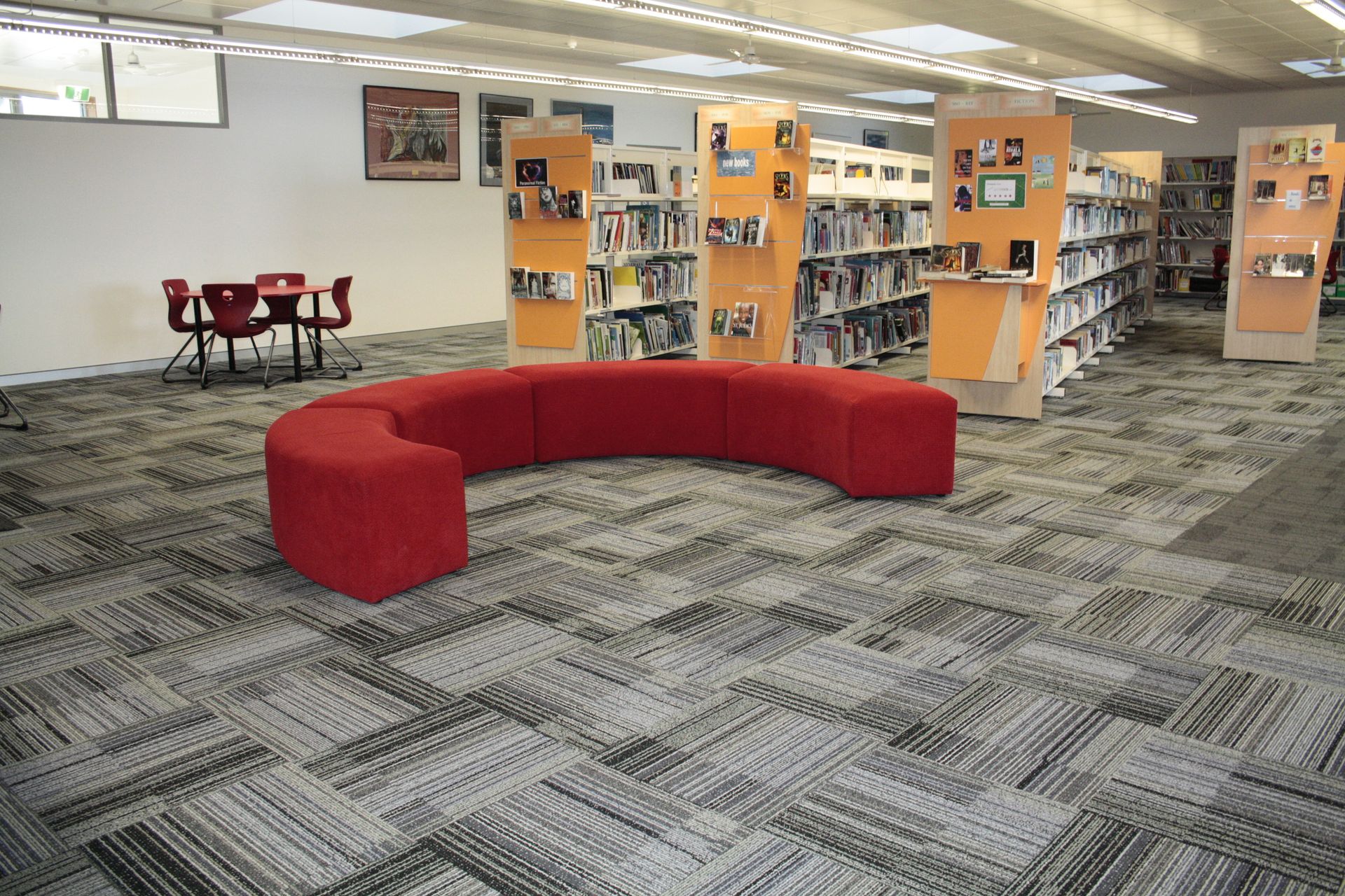 Library interior with red curved sofa, patterned carpet, and bookshelves — Unique Floors In New Town, TAS