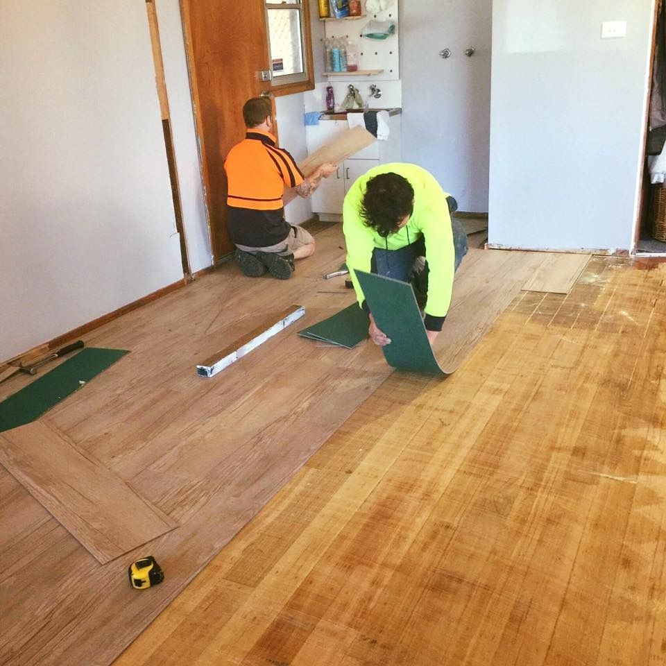 Two Workers Installing Hardwood Flooring in a Room, One Kneeling and One Bending Over Green Boards — Unique Floors In New Town, TAS