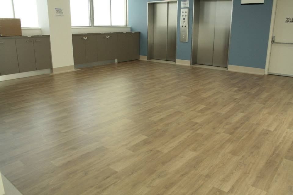 Empty Room With Light Wood Flooring, Windows, Cabinets, and Two Elevators Along the Wall — Unique Floors In New Town, TAS