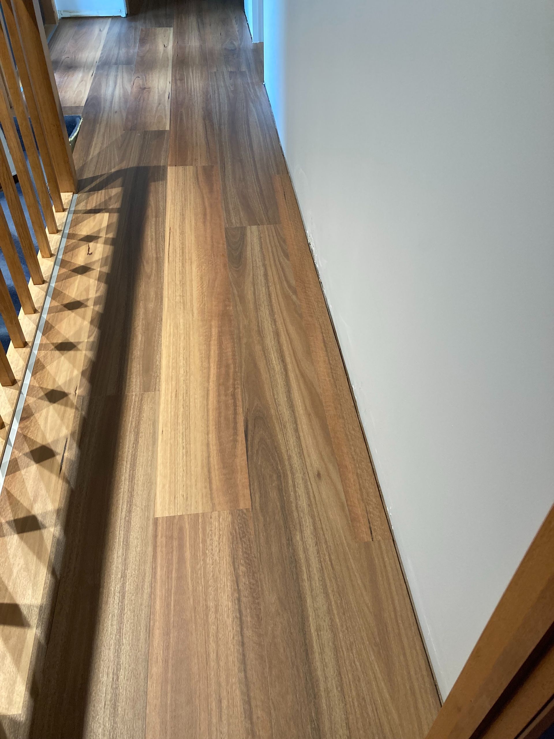 Narrow Wooden Hallway With Sunlight on the Floor, White Walls, and a Stair Railing on the Left — Unique Floors In New Town, TAS