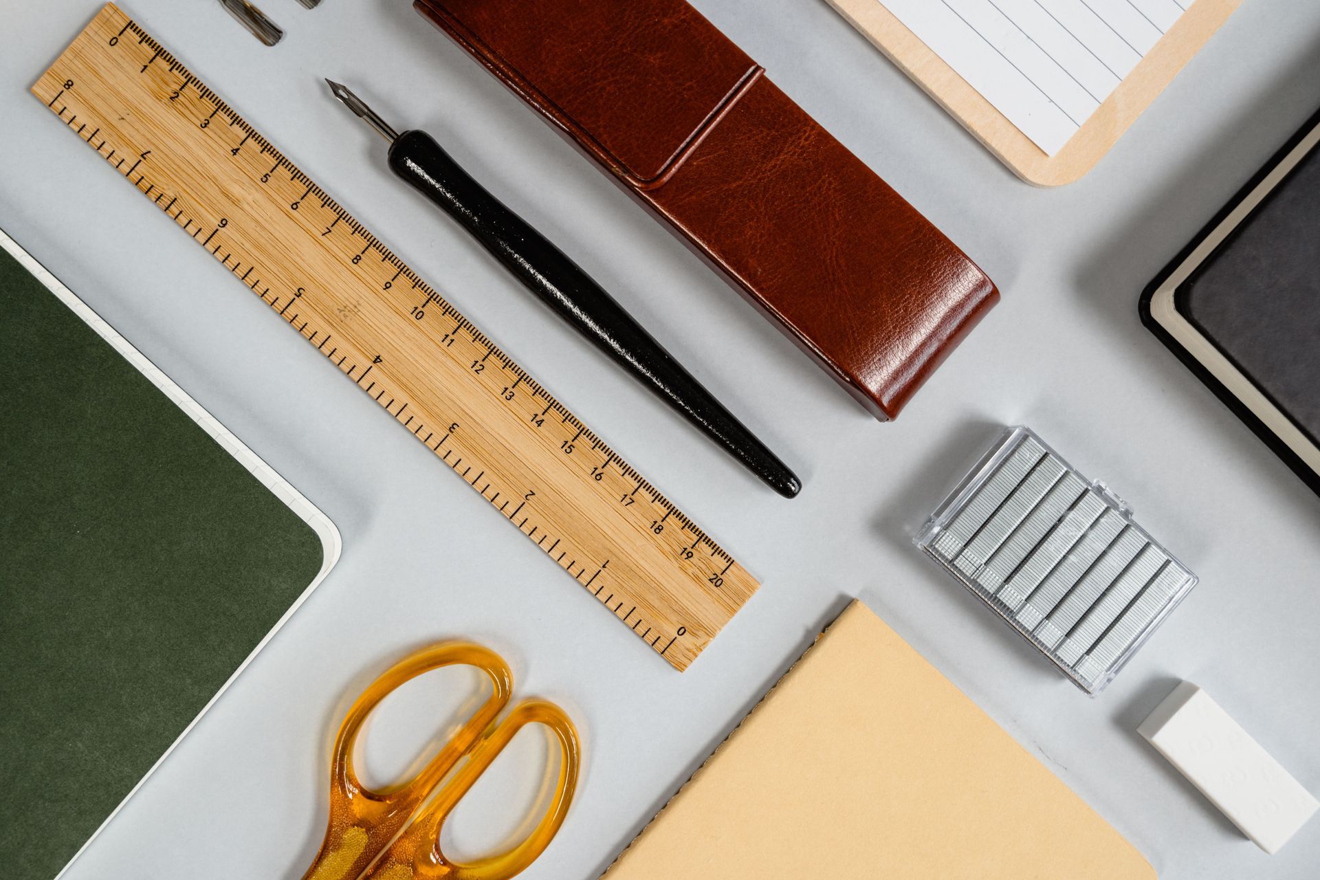 Vista cenital de material de papelería sobre un escritorio gris claro: cuadernos, lápiz, regla, tijeras y bolígrafo.