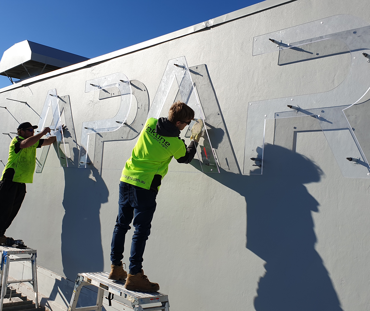 Two men are standing on a ladder painting letters on a wall. Two men are standing on a ladder painting letters on a wall.