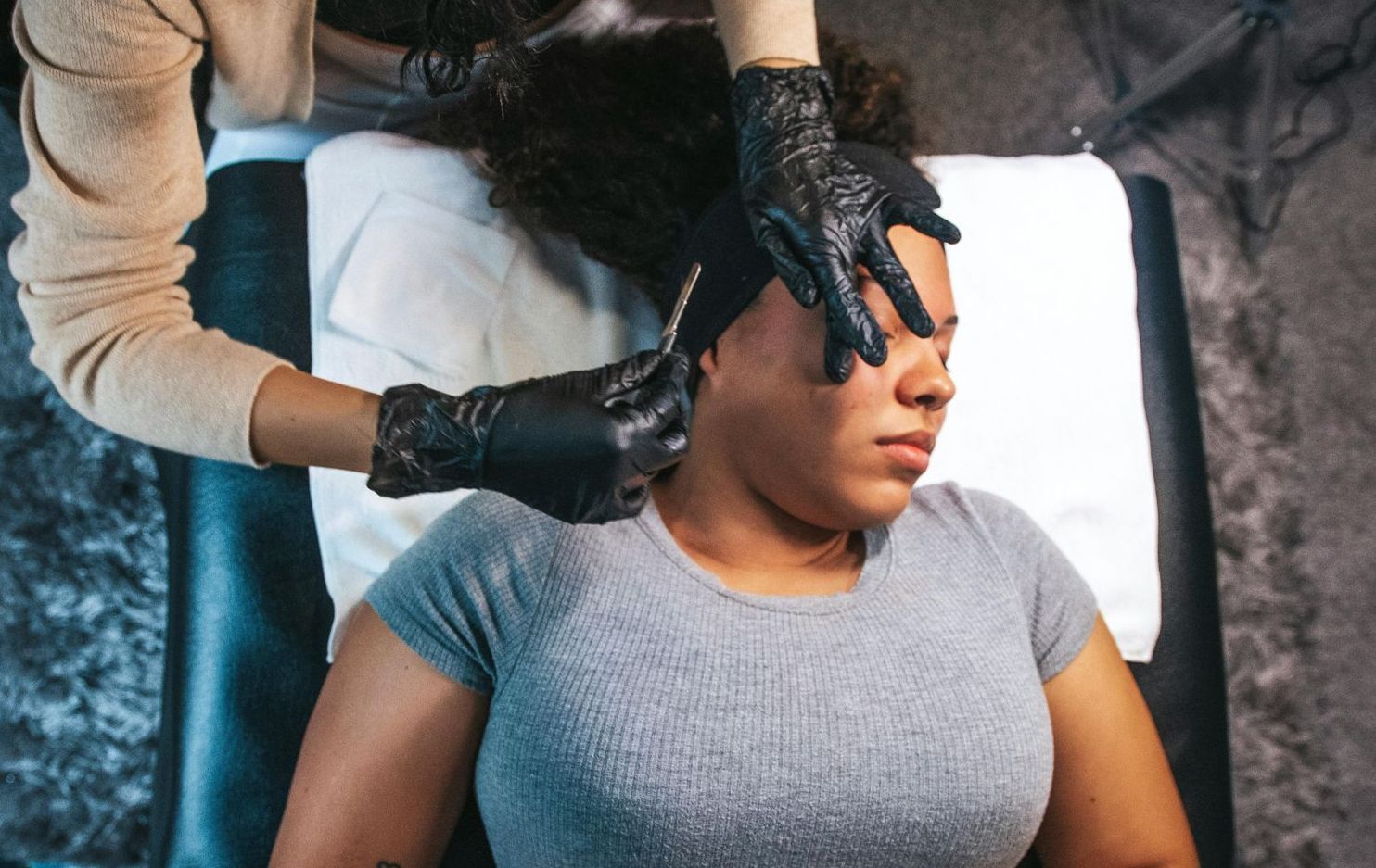 A woman is laying on a bed getting a tattoo on her face.