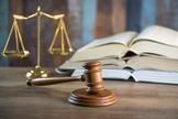 Gavel on wooden surface, with balanced scales and open books in the background.