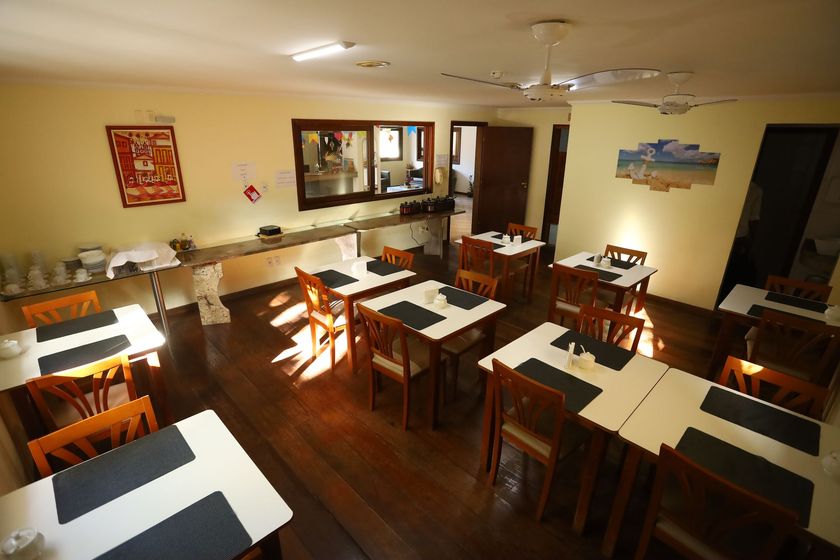 Sala de jantar vazia de um restaurante com mesas e cadeiras de madeira, e a luz quente do sol incidindo sobre um piso polido.