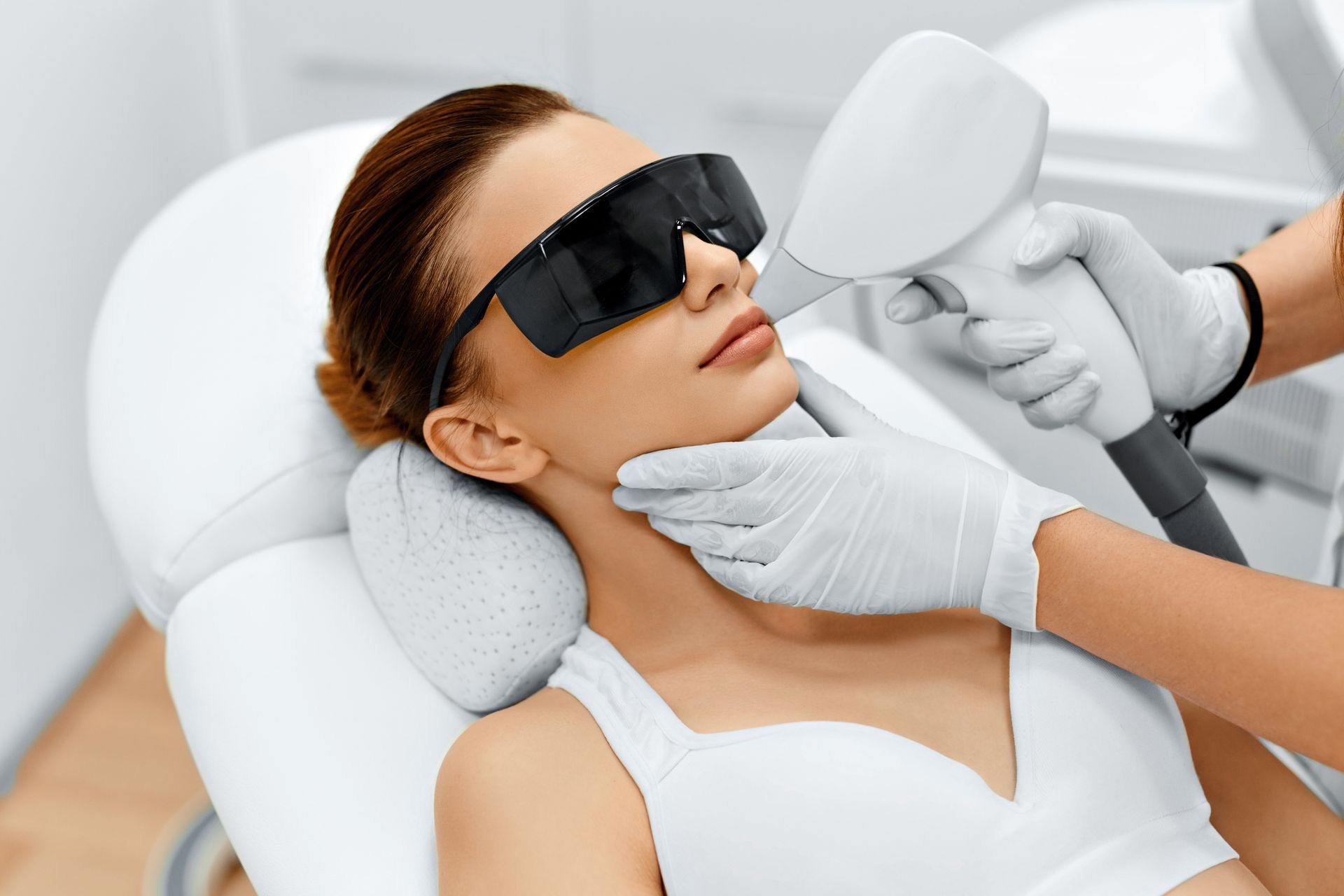 Woman with freshly microbladed eyebrows smiles while lying down on a white paper-covered table.