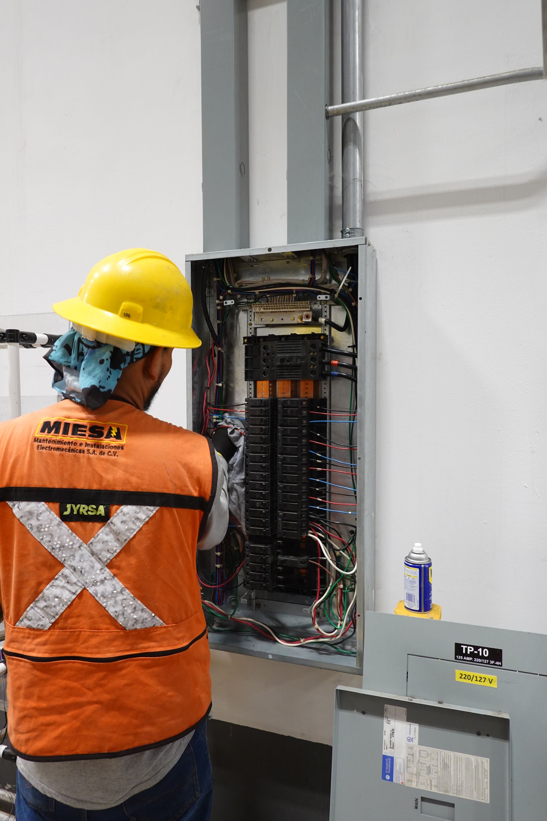 Un hombre que lleva un casco y un chaleco naranja está trabajando en una caja eléctrica.