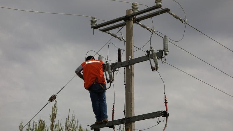 Un hombre está parado encima de un poste eléctrico.