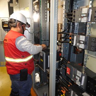 Un hombre con un chaleco rojo está trabajando con equipos eléctricos.