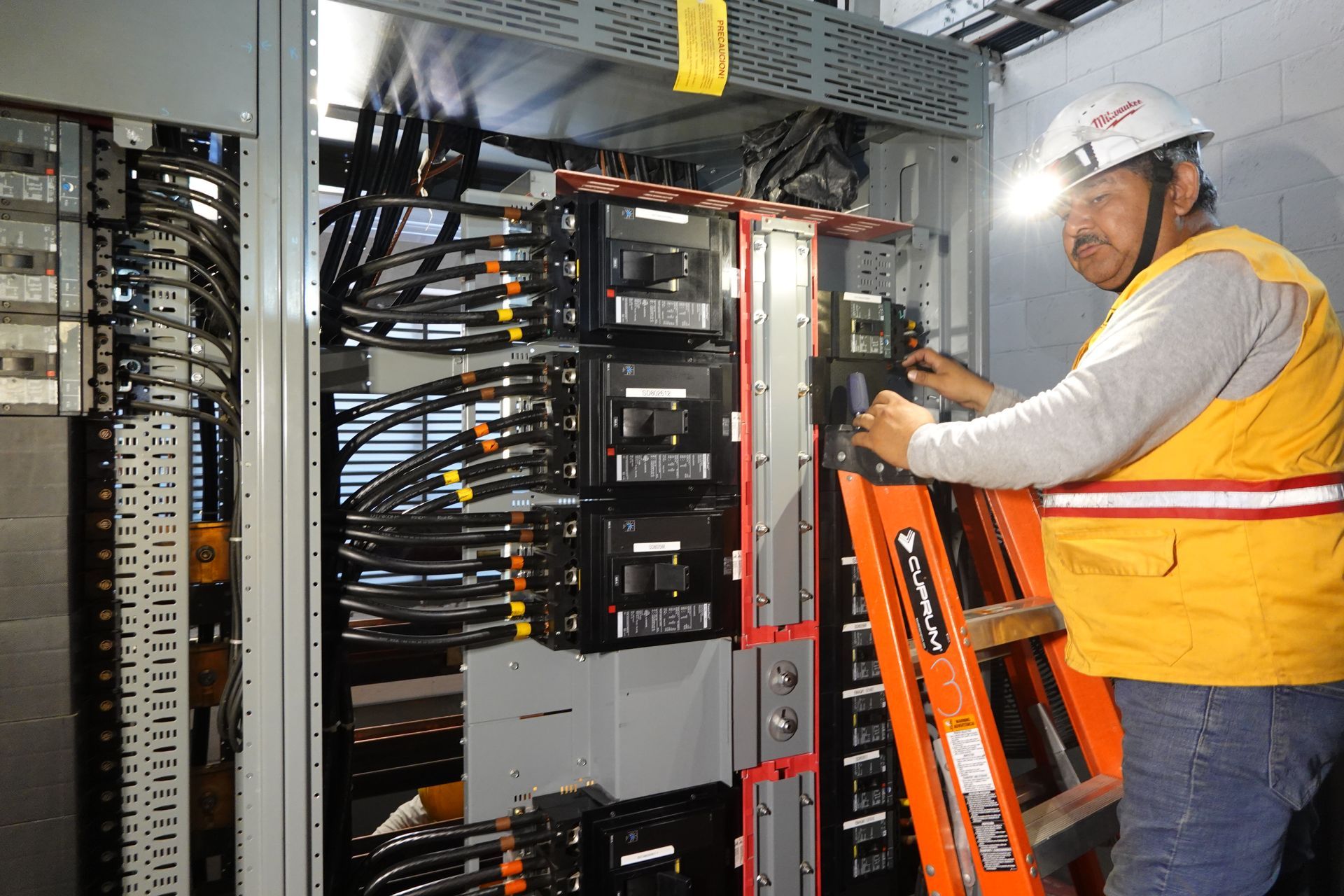 Un hombre está de pie en una escalera trabajando en una caja eléctrica.