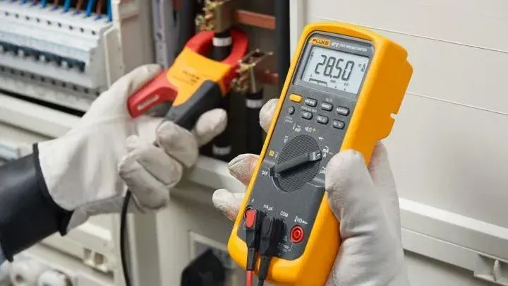 A person is holding a digital multimeter in their hands.