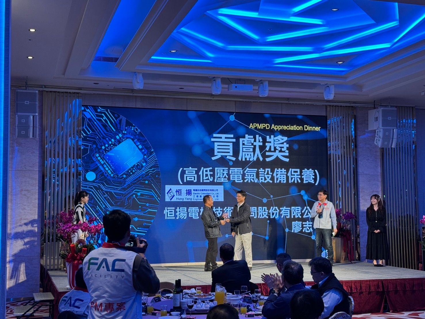 A group of people are standing on a stage in front of a large screen.