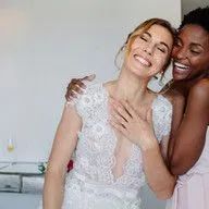 A bride and her bridesmaid are hugging each other and smiling.