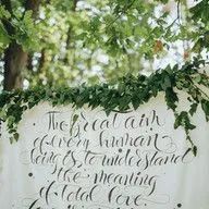 A sign with a quote on it is hanging from a tree.