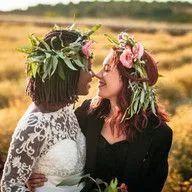 Two women wearing flower crowns are kissing in a field.