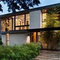A modern house with a lot of windows and trees in front of it.