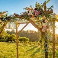 A wooden arch decorated with flowers and leaves in a field.