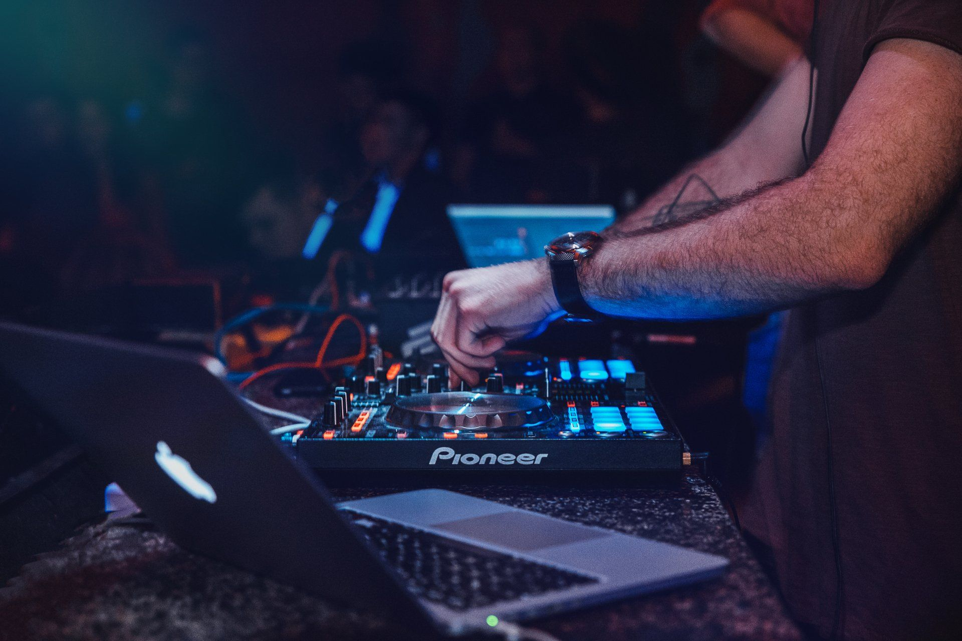 A man is playing music on a pioneer dj controller while using a laptop.