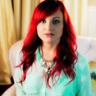 A woman with red hair is sitting in a chair wearing a green shirt and a necklace.