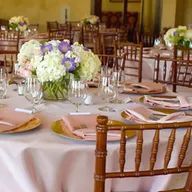 A table set for a wedding reception with plates , glasses , and flowers on it.