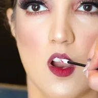 A woman is applying lipstick to her lips with a brush.