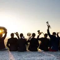 A group of men are sitting on the ground playing instruments.