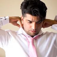 A man in a white shirt and pink tie is adjusting his tie.