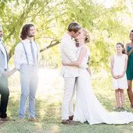 A bride and groom are kissing in front of their wedding party.