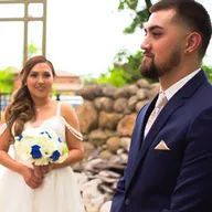 A bride and groom are standing next to each other in front of a stone wall.