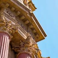 A close up of a building with columns and a blue sky in the background.