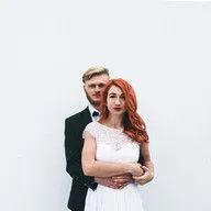 A bride and groom are posing for a picture in front of a white wall.