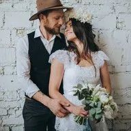 A bride and groom are posing for a picture in front of a white brick wall.
