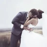 A bride and groom are kissing in a field on their wedding day.