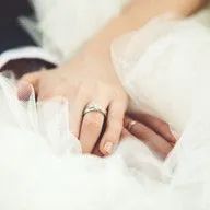 A bride and groom are holding hands with wedding rings on their fingers.