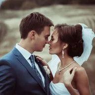 A bride and groom are kissing in a field on their wedding day.
