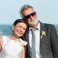 A bride and groom are posing for a picture on the beach.