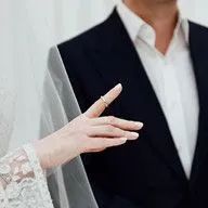 A bride and groom are standing next to each other and the bride is wearing a wedding ring on her finger.