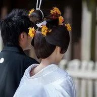 A man and a woman are standing next to each other and the woman has flowers in her hair.